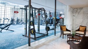 A gym with exercise equipment, a seating area with chairs, and a large window offering a view of the gym.