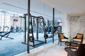 A gym with exercise equipment, a seating area with chairs, and a large window offering a view of the gym. - Crowne Plaza Beijing Chaoyang U-Town by IHG (Beijing)