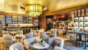 A bar area with a variety of bottles, a seating area with round tables and chairs, and a decorative ceiling light.