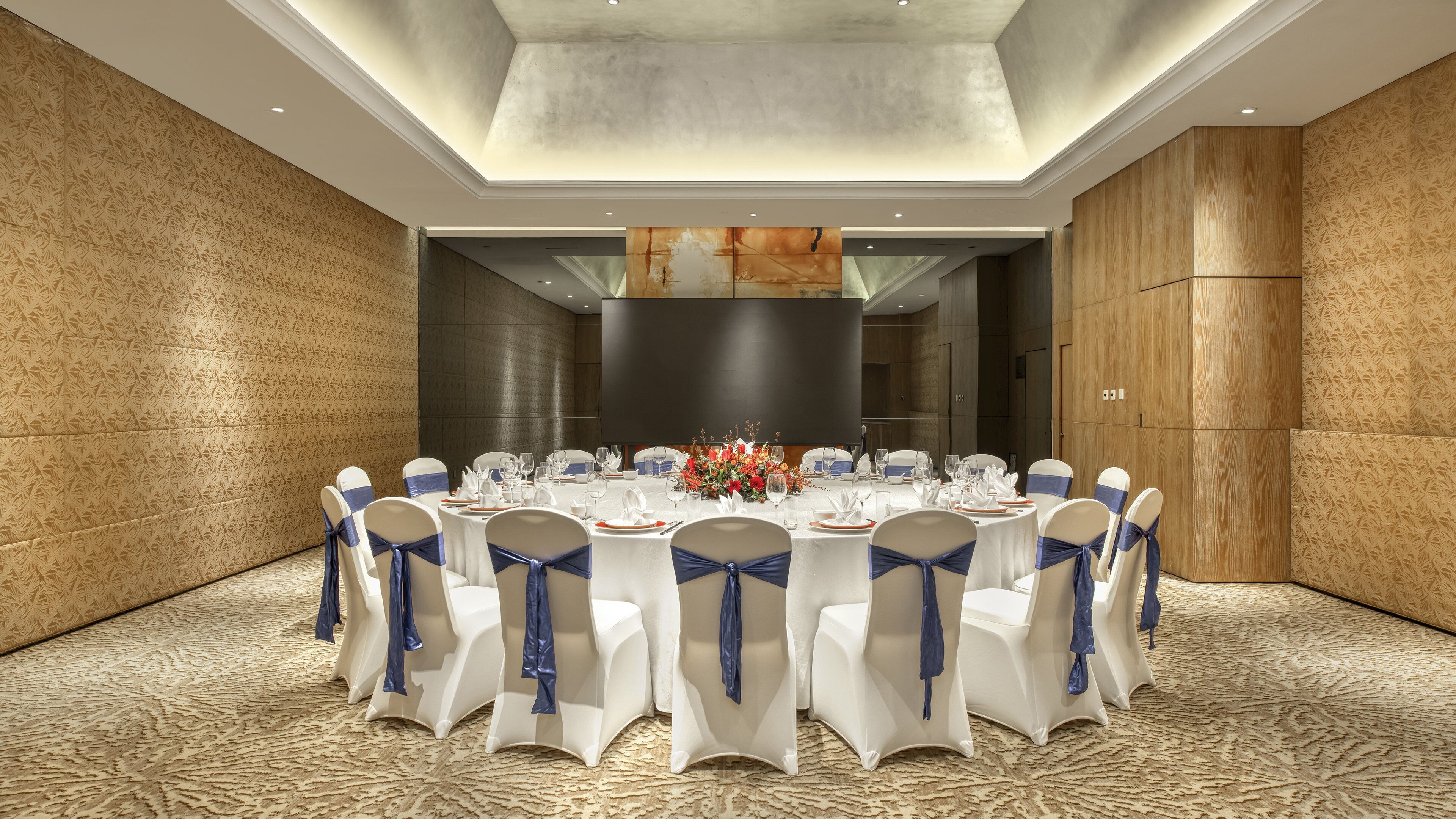 A conference room with a round table, white chairs with blue sashes, and a floral centerpiece.