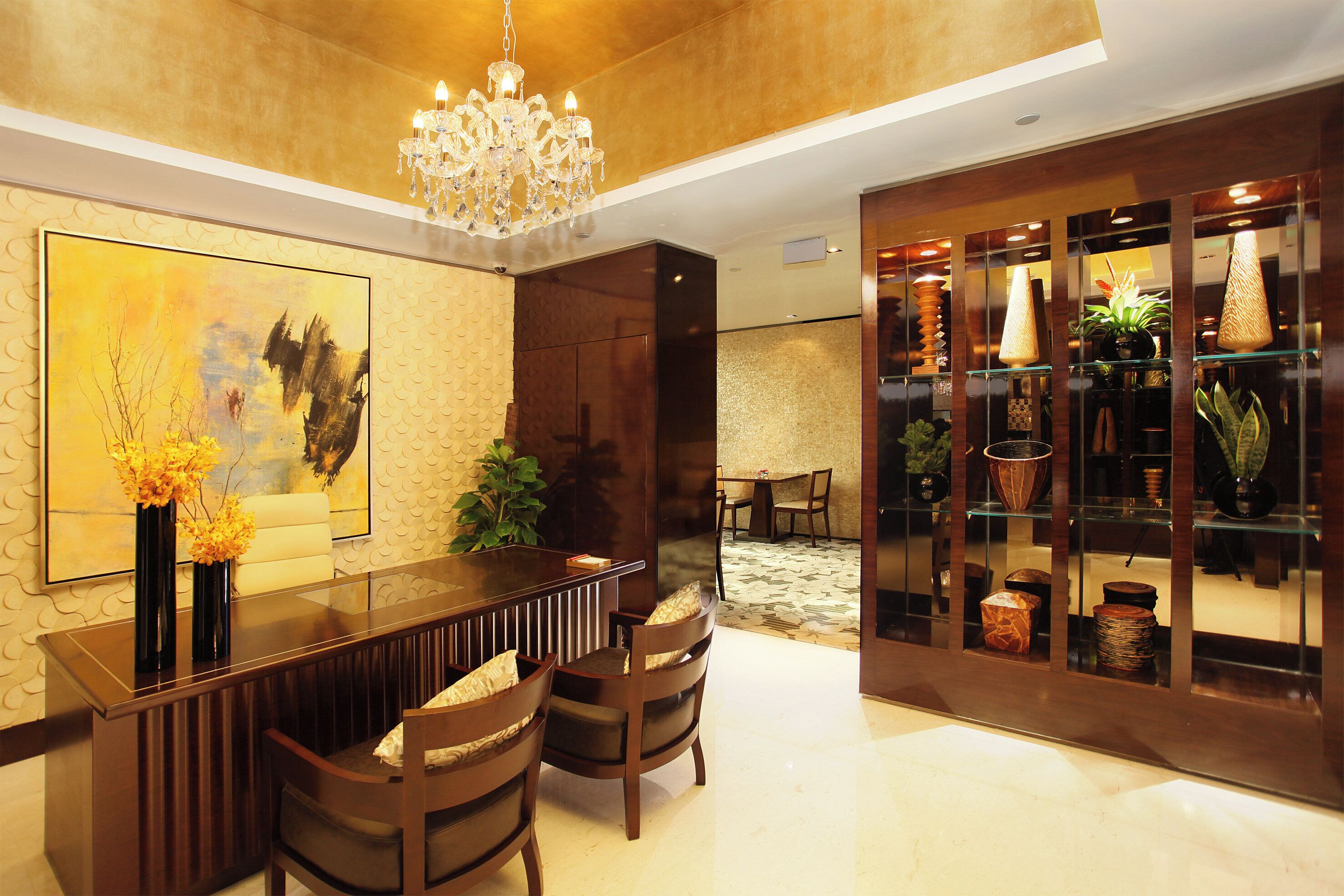 Un interior moderno con una zona de bar, asientos, una araña y un aparador con objetos decorativos.