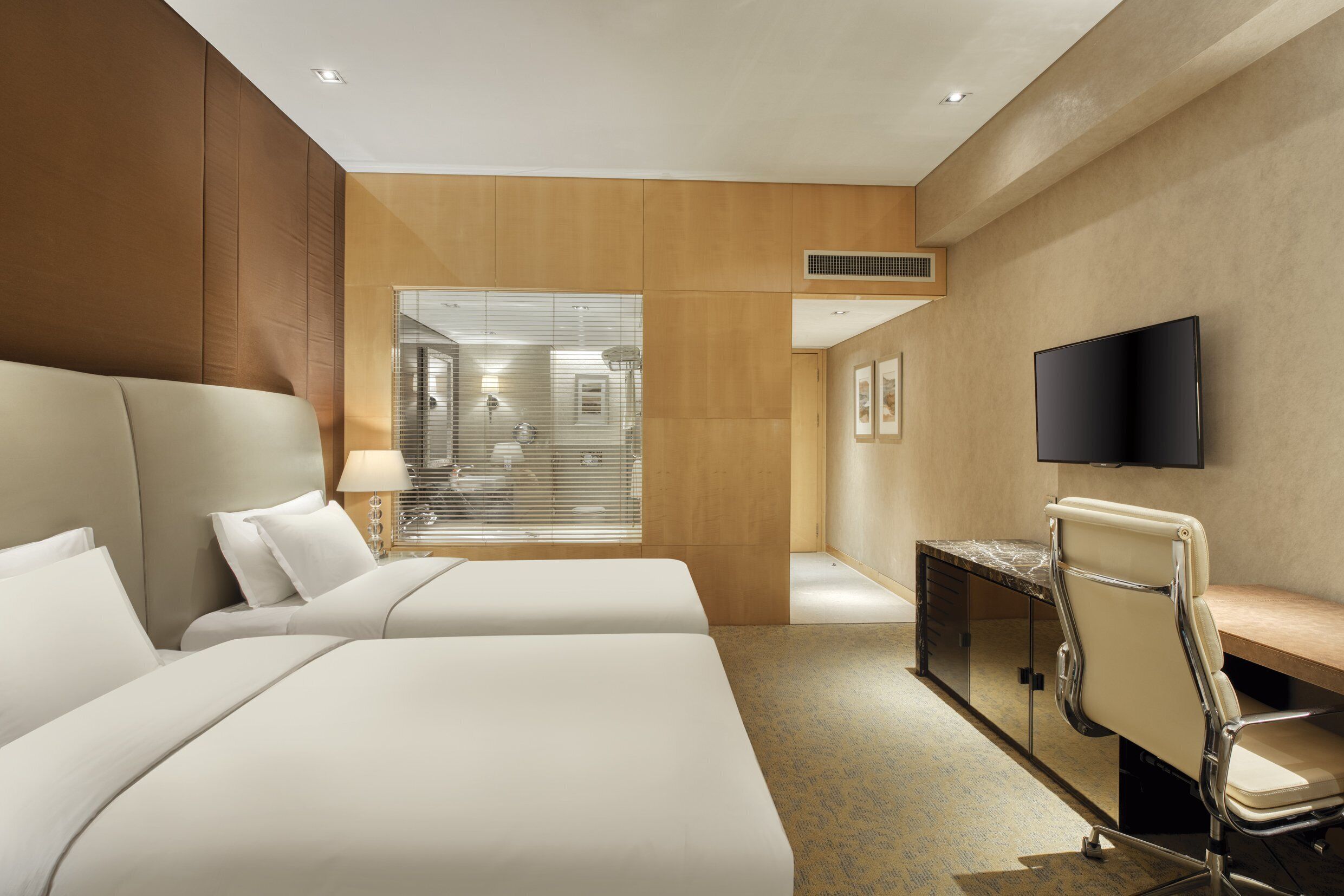 Habitación de hotel con dos camas, un escritorio, una silla, un televisor y una ventana con persianas.
