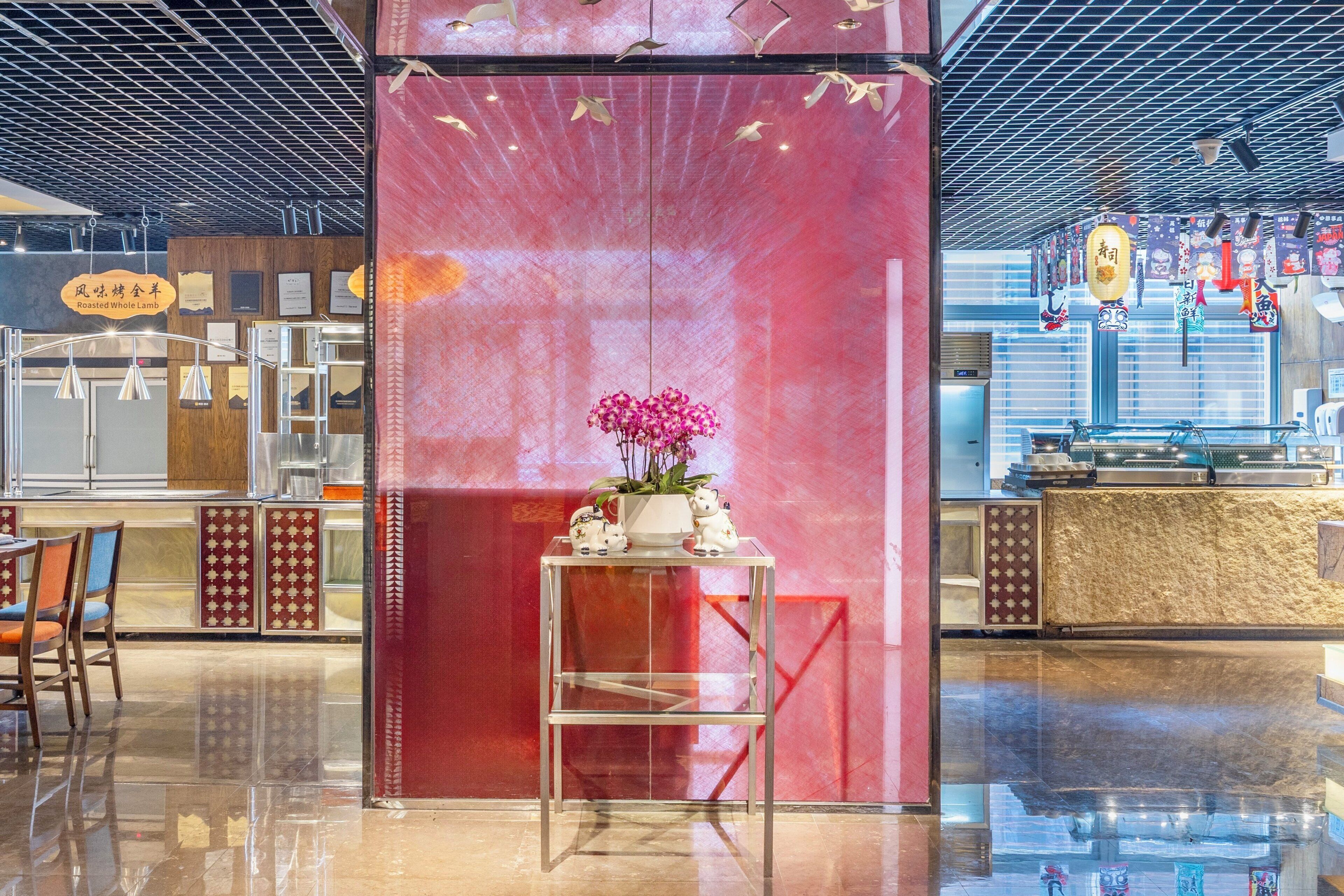 Interior de un restaurante con una pared de acento roja, una mesa de vidrio con un arreglo floral y una barra de sushi al fondo.