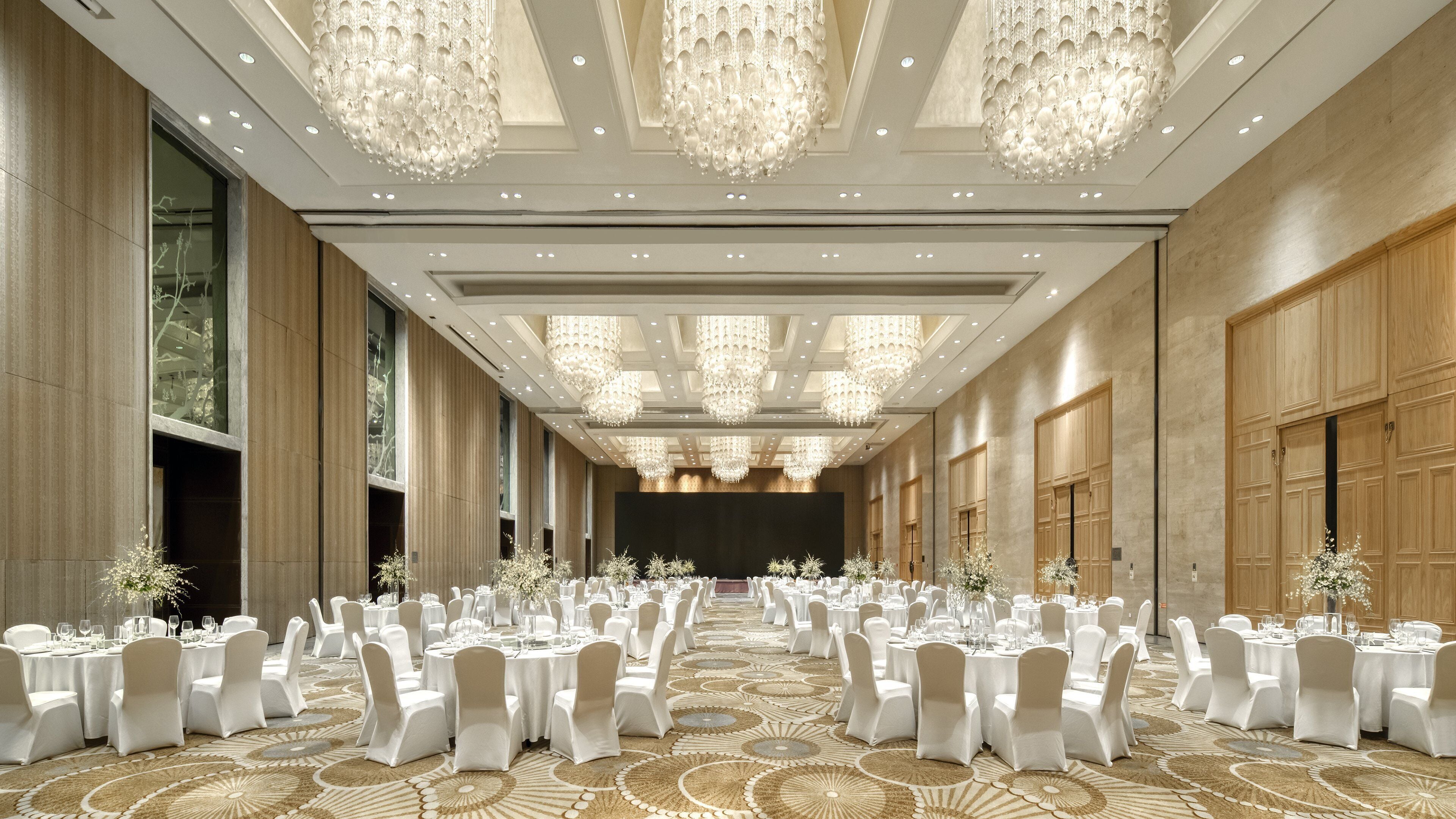 A banquet hall with round tables, white chairs, and chandeliers.