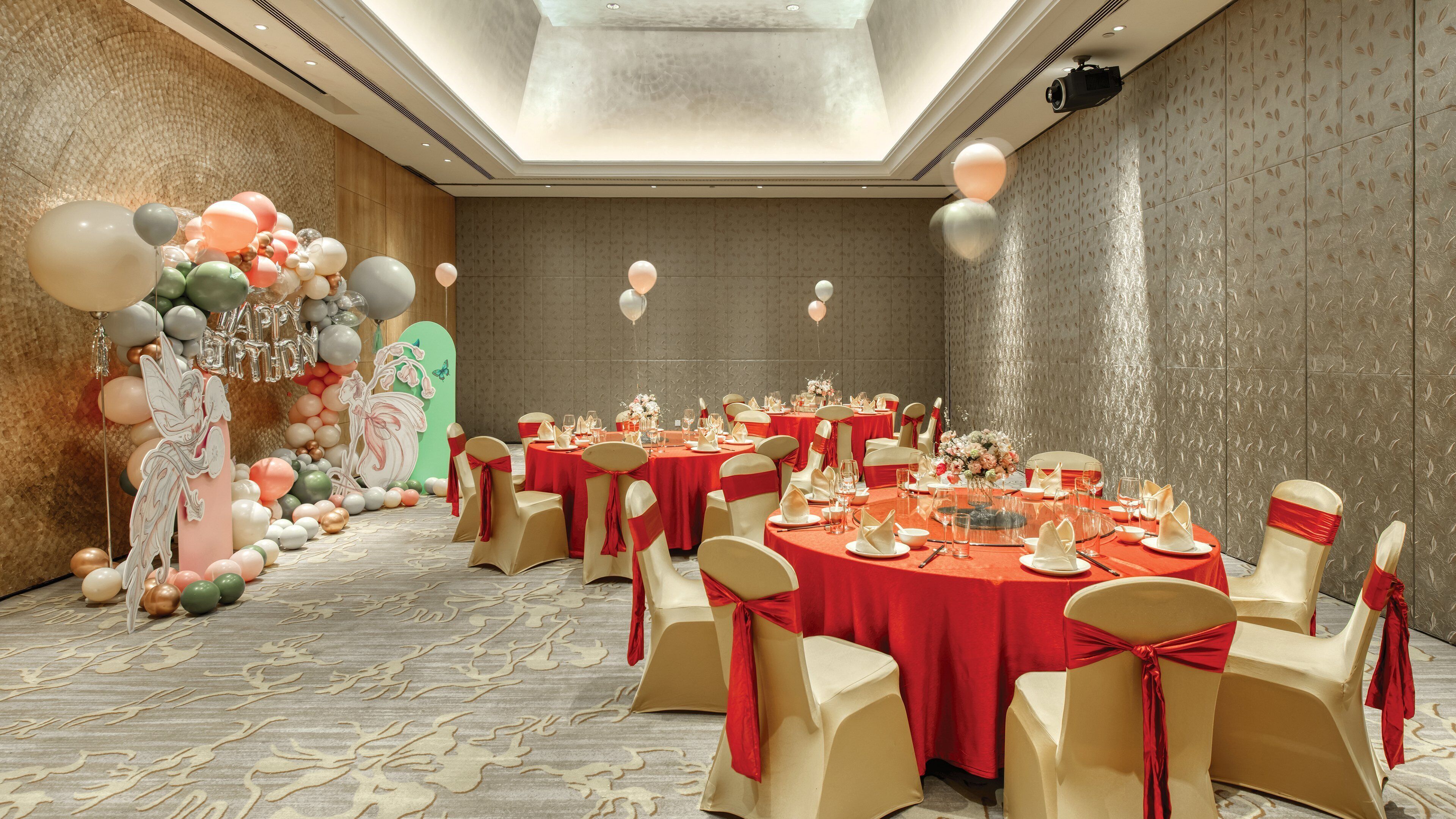 A banquet hall with round tables, red tablecloths, and chairs with red sashes.