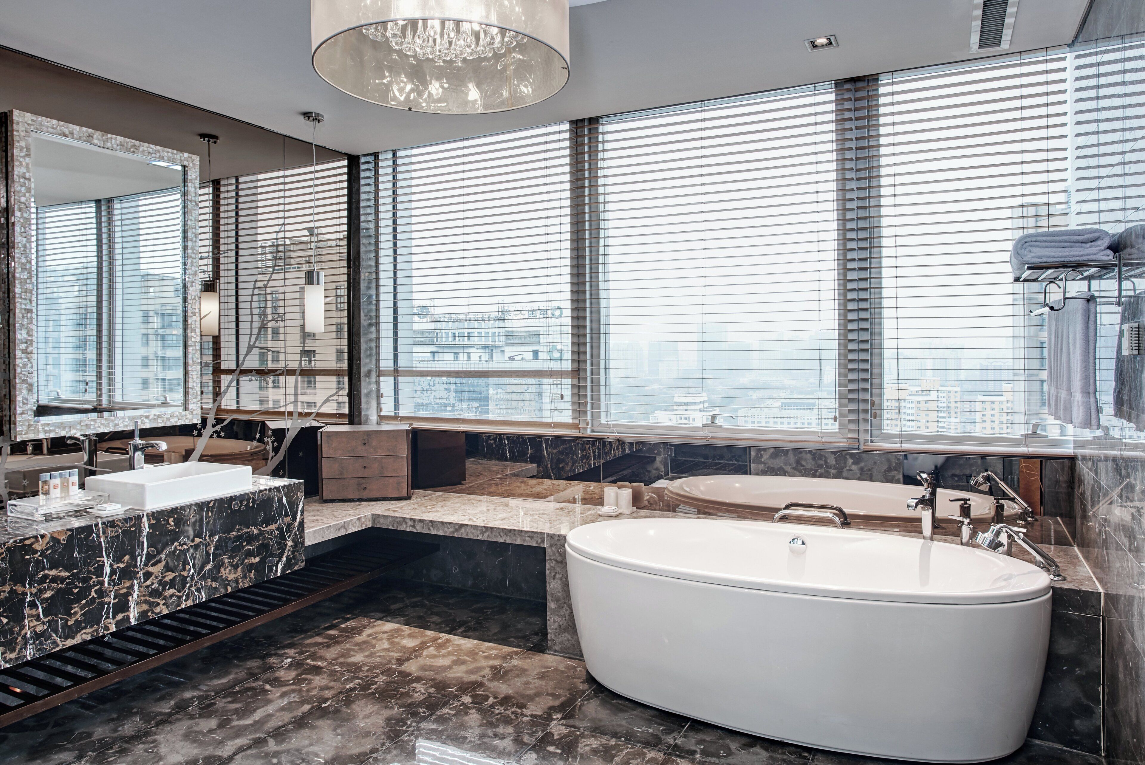 A modern bathroom with a large bathtub, a vanity with a marble countertop, and a large mirror.