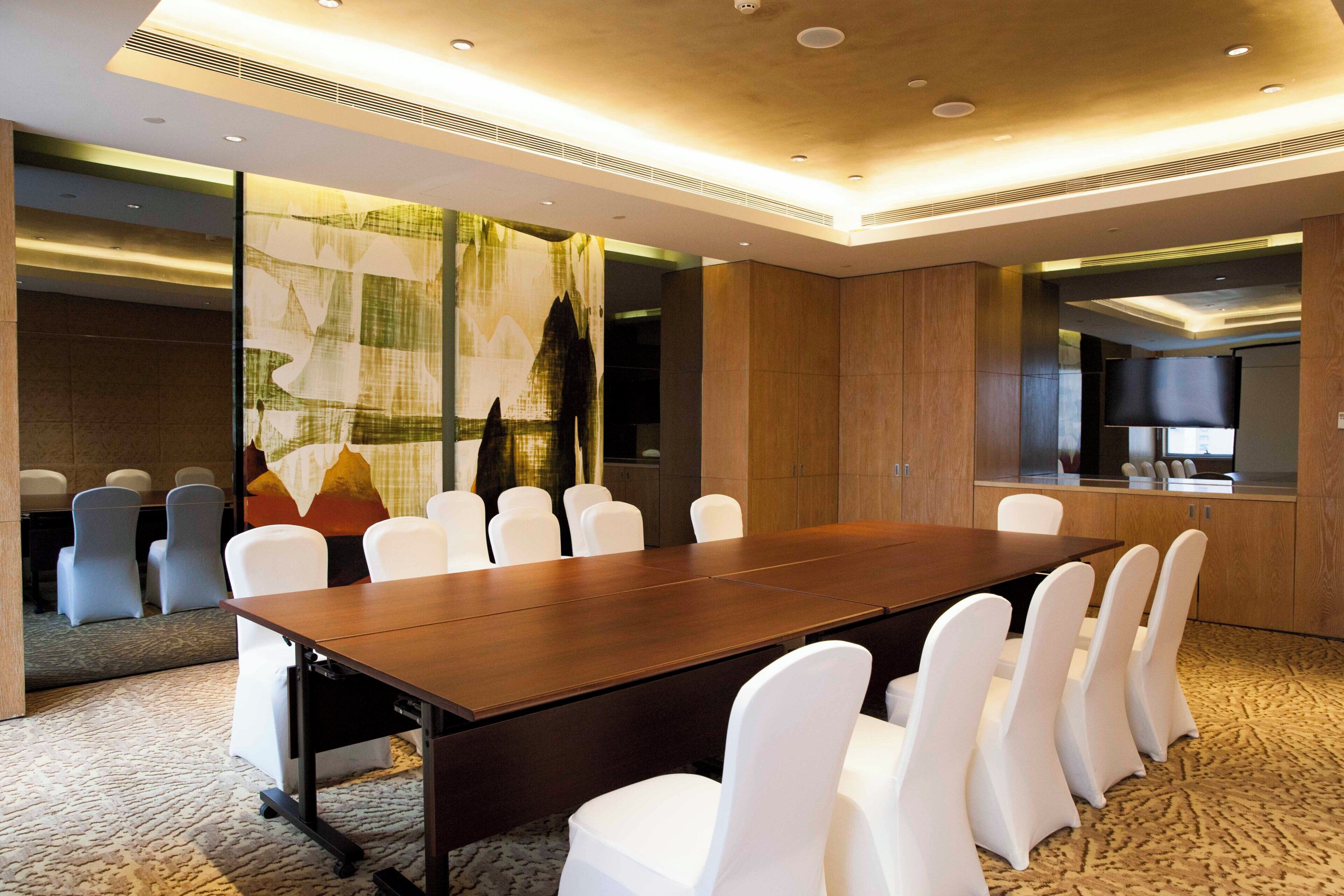A conference room with a long table and white chairs, a large window with a view, and a modern ceiling design.