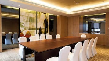 A conference room with a long table and white chairs, a large window with a view, and a modern ceiling design.