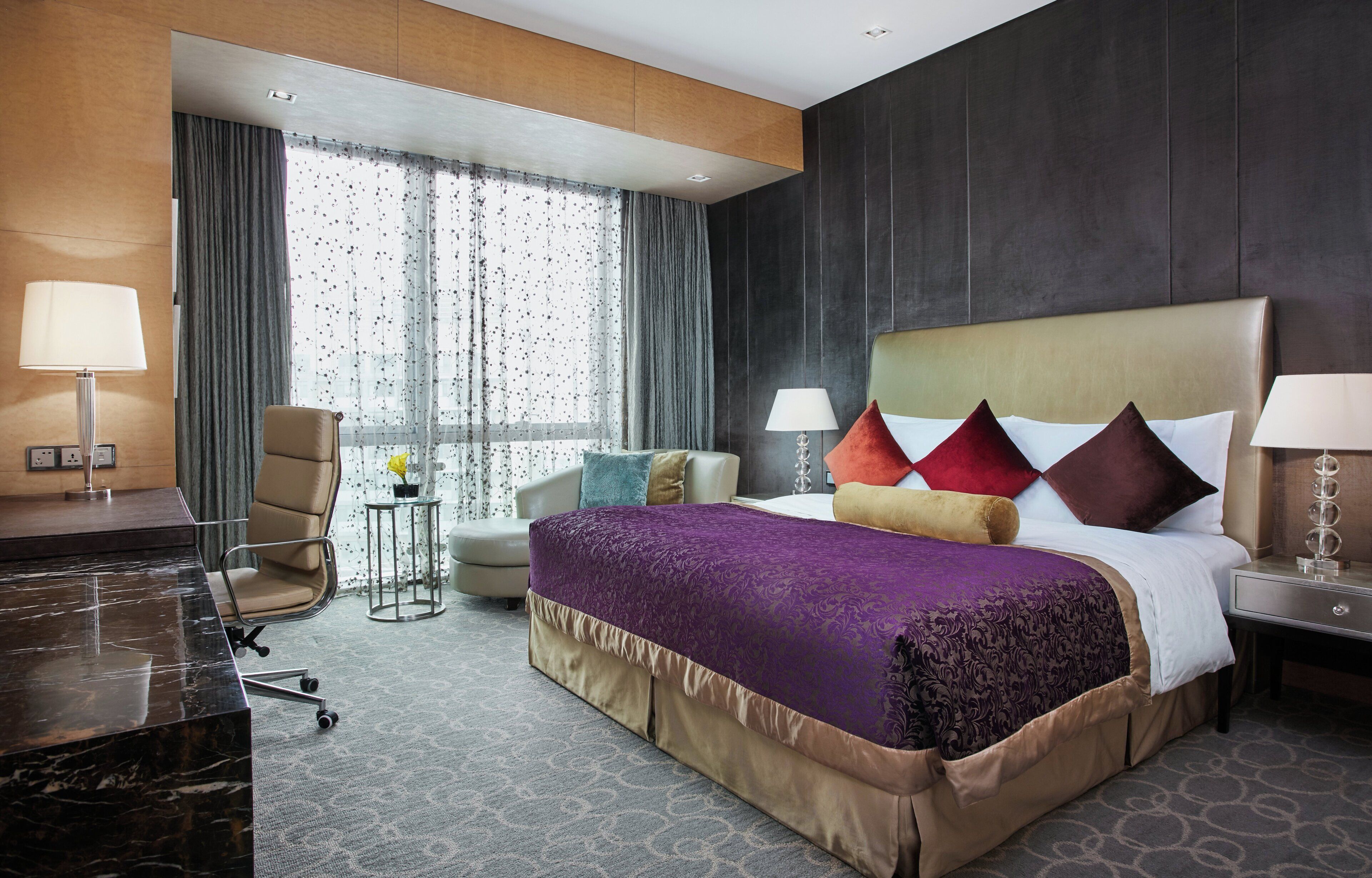 Habitación de hotel con una cama grande, un escritorio, una silla, una mesita y una ventana con cortinas.
