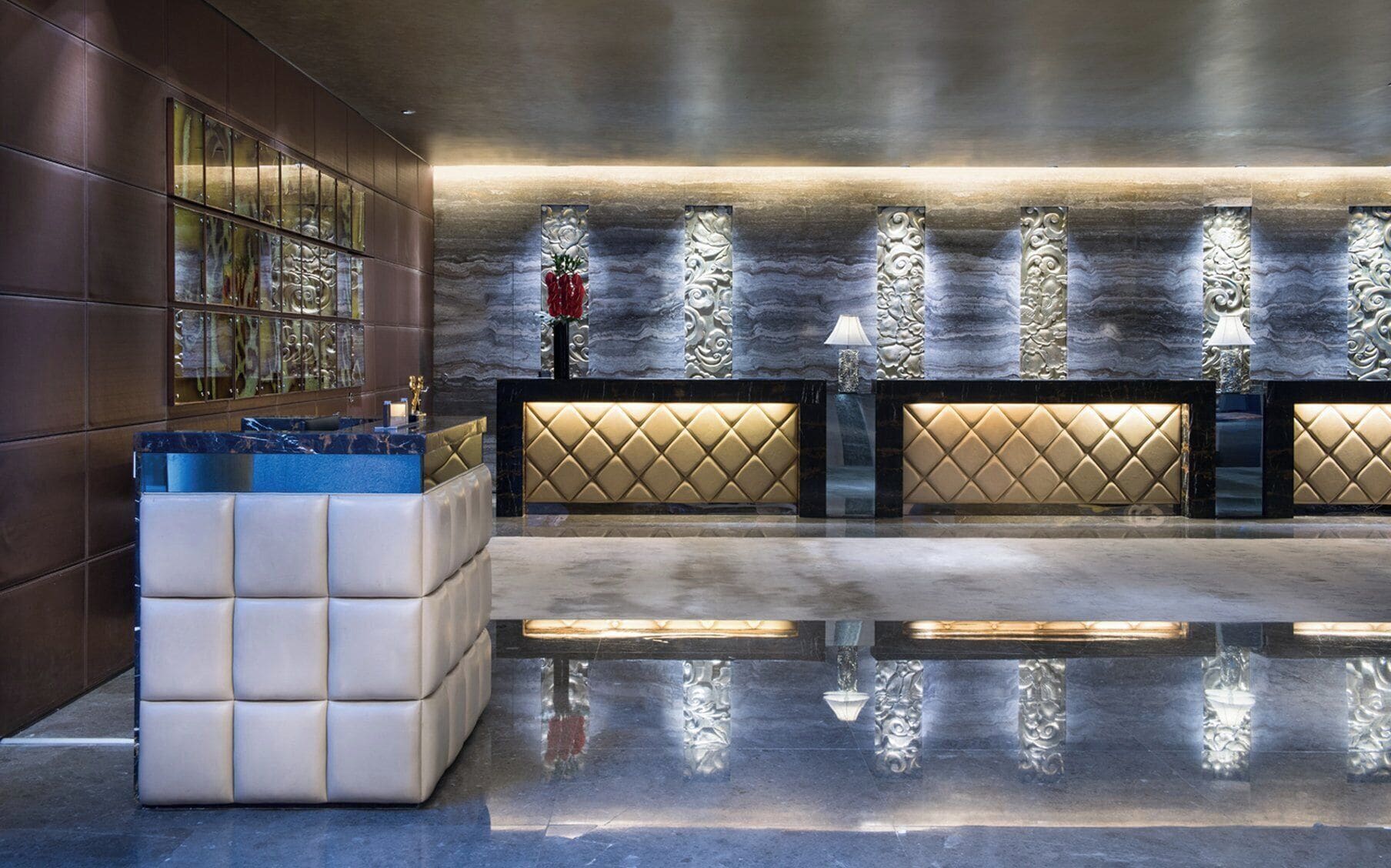 A modern reception area with a marble reception desk, a seating area with cushioned chairs, and a glass display case.