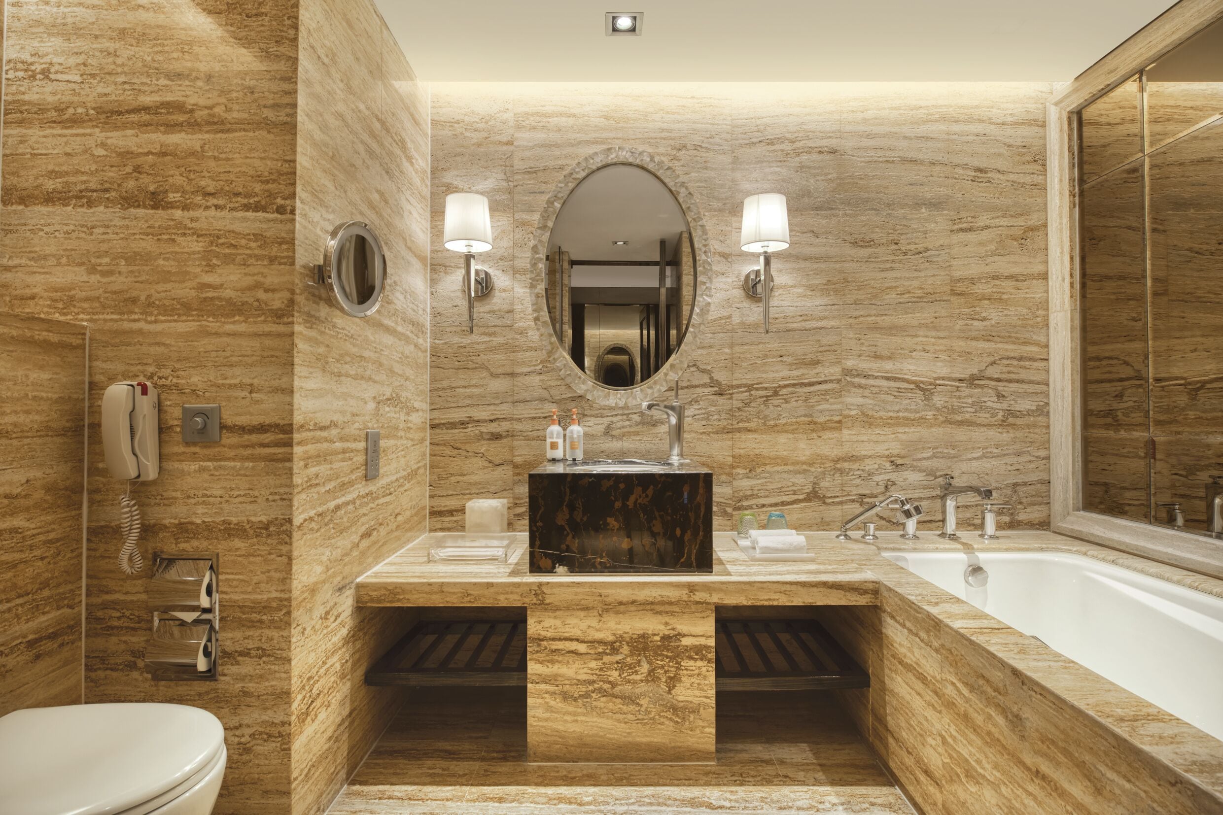 A modern bathroom with a marble wall, a large mirror, a sink, and a bathtub.