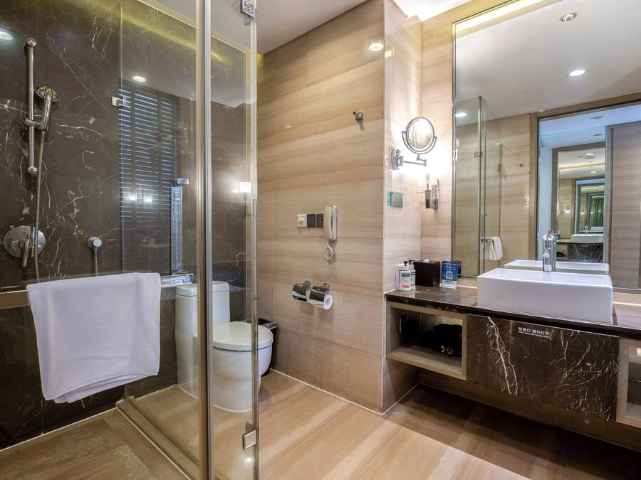 Een moderne badkamer met een douchecabine van glas, een toilet, een wastafel met spiegel en een badkamermeubel.
