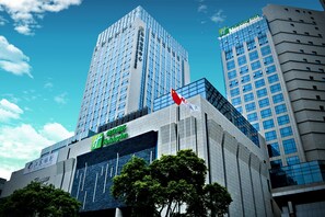 A modern hotel building with a prominent flag, large windows, and a sign for Holiday Inn. - Holiday Inn Shanghai Songjiang by IHG (Shanghai)