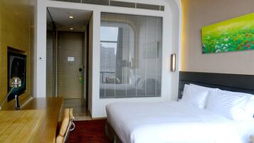 A hotel room with a bed, a desk, a chair, a painting, and a door leading to a bathroom.