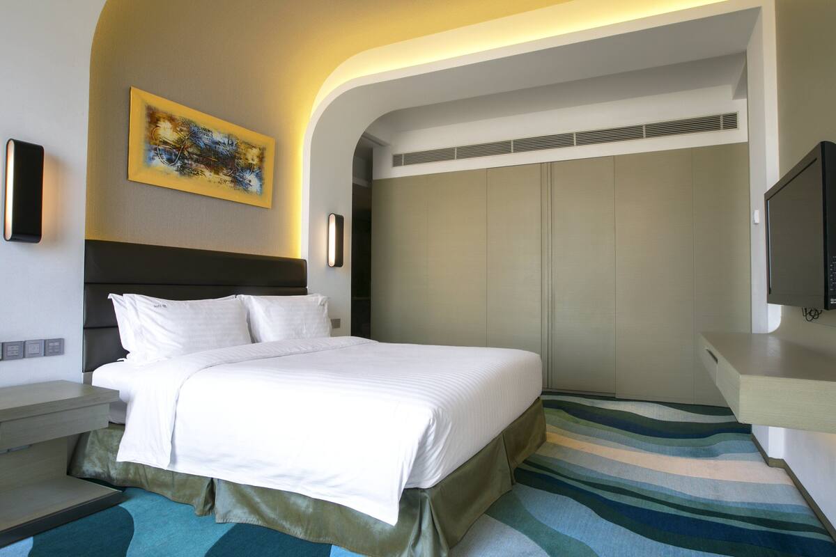 A modern hotel room with a large bed, a flat-screen TV, a painting on the wall, and a wardrobe.
