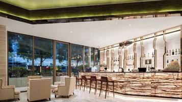 Zona de bar moderna con encimera de mármol, taburetes y un amplio ventanal con vistas al exterior.