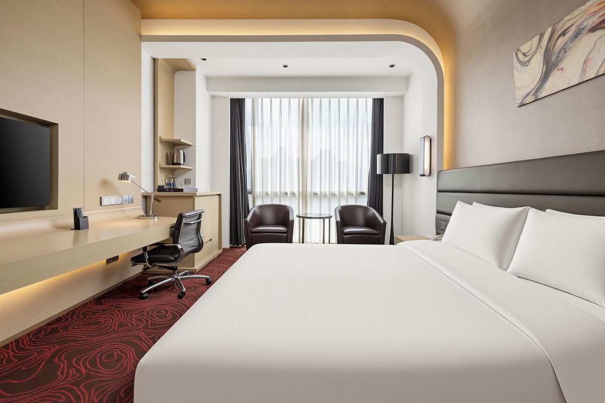 Een hotelkamer met een groot bed, een bureau, twee stoelen, een televisie en een schilderij aan de muur.