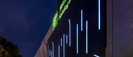 Un hotel con un llamativo letrero de neón, amplias columnas y una entrada espaciosa.
