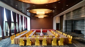 Une salle de conférence avec une longue table, des chaises jaunes et un lustre.