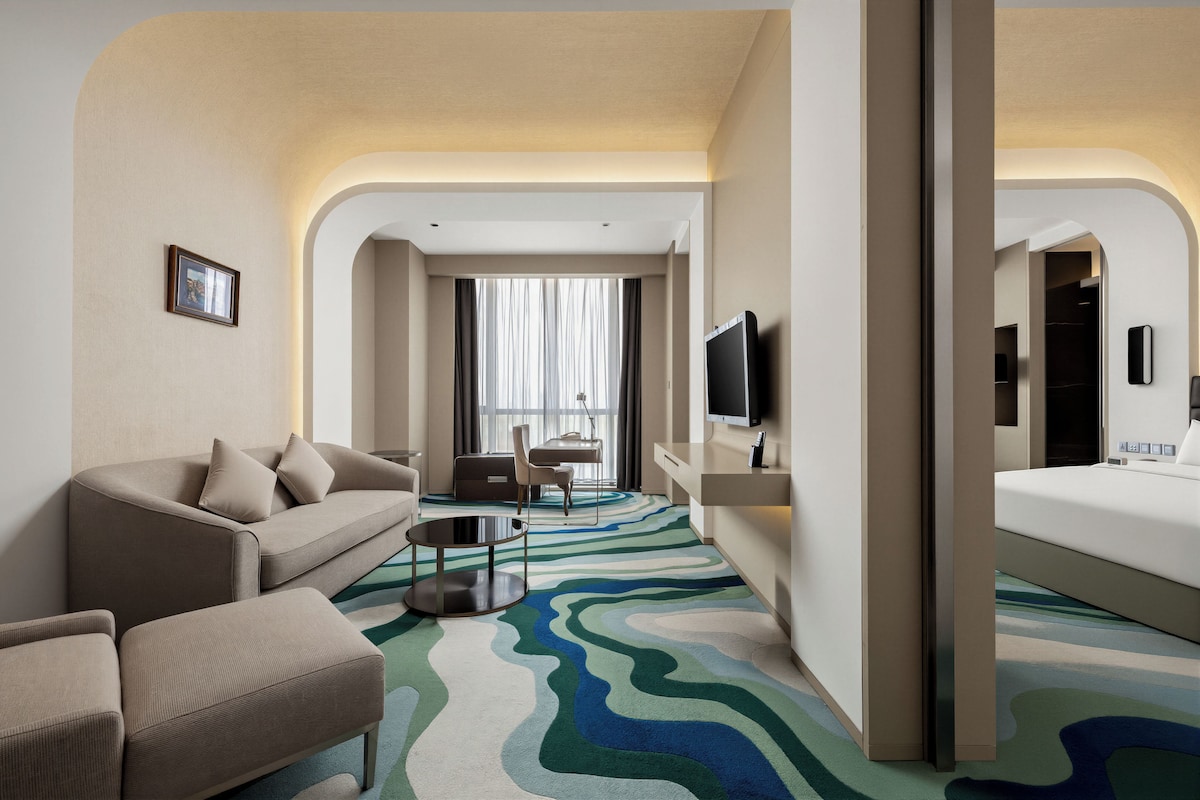 Een hotelkamer met een bank, een klein tafeltje, een televisie, een bed en een badkamer, zichtbaar via een boog.
