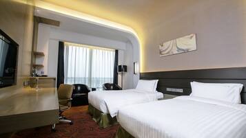 A hotel room with two beds, a desk, a chair, a TV, and a window with curtains.