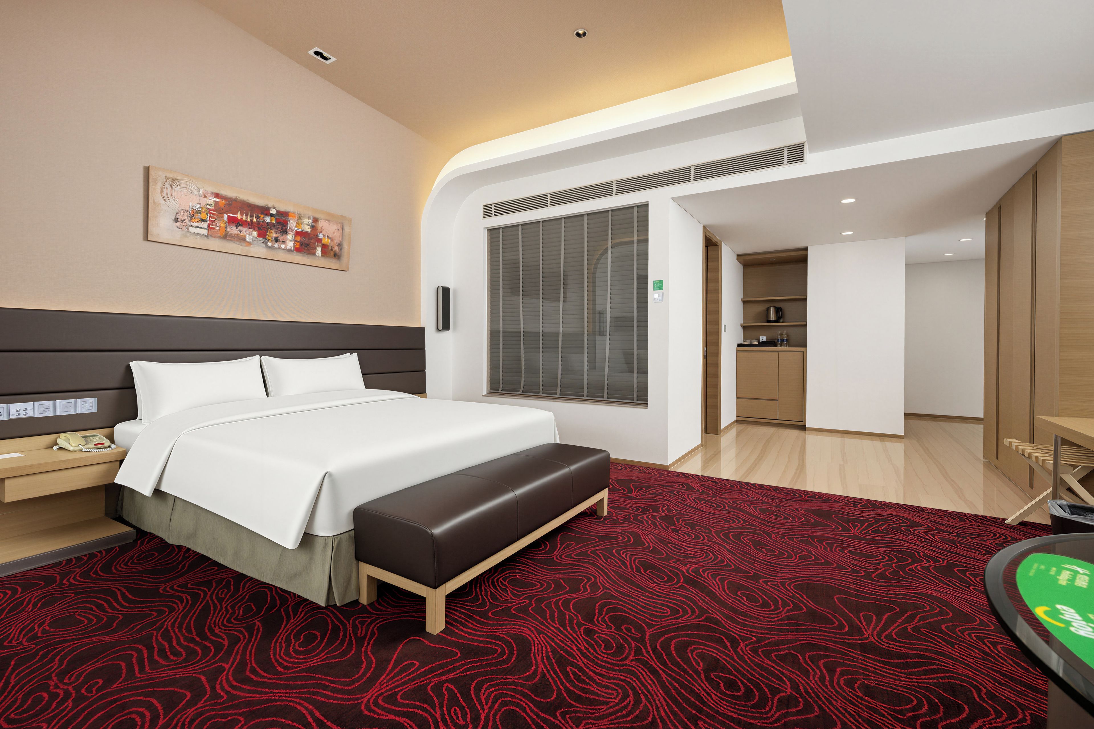Habitación de hotel moderna con una cama grande, un escritorio, un banco, un cuadro y vista a la cocina.