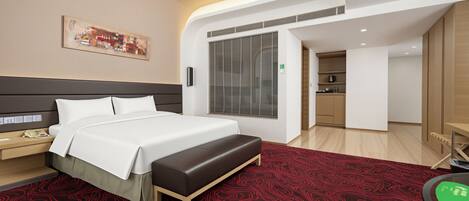 Habitación de hotel moderna con una cama grande, un escritorio, un banco, un cuadro y vista a la cocina.
