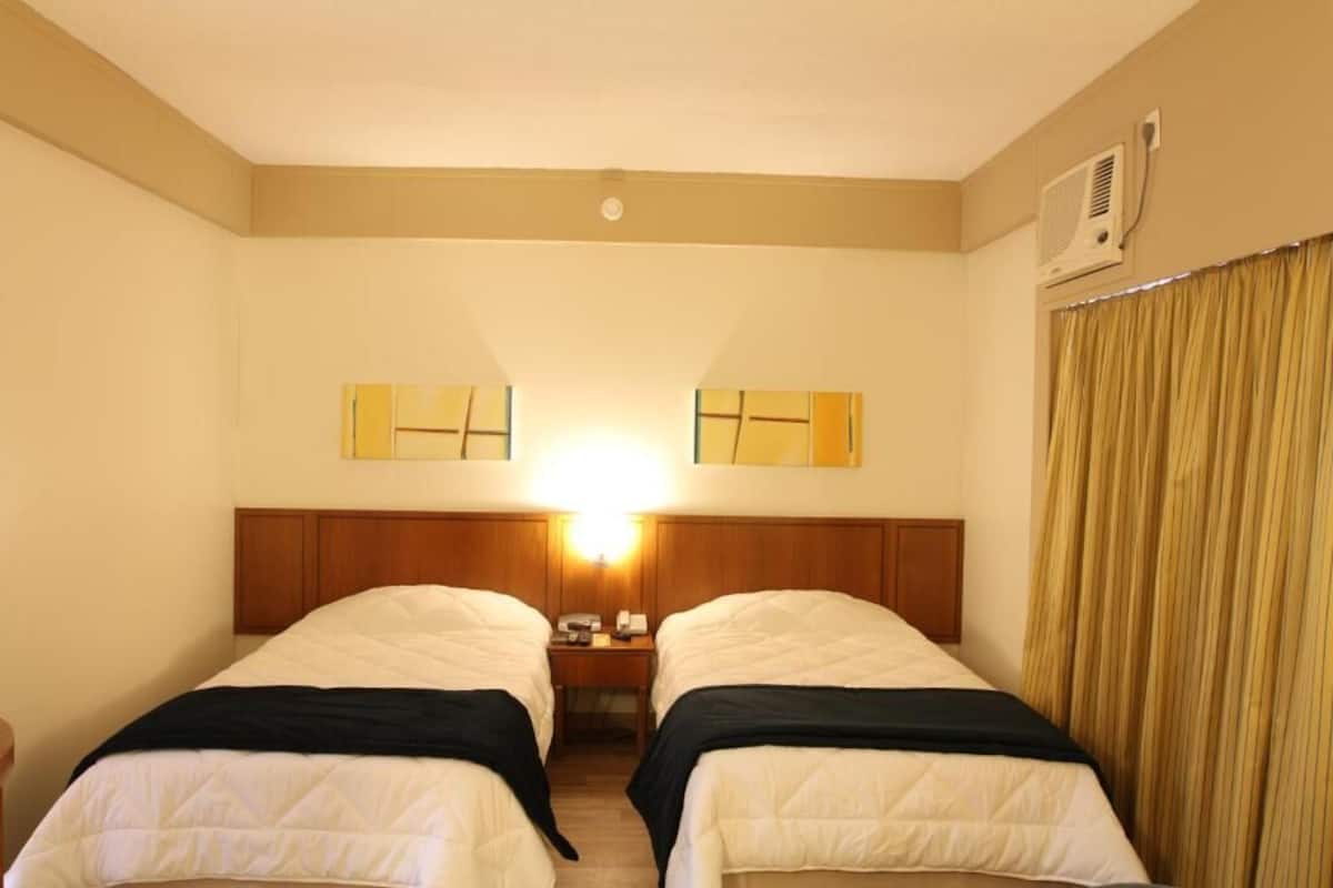 A hotel room with two beds, a wooden headboard, a nightstand, and a mirror.