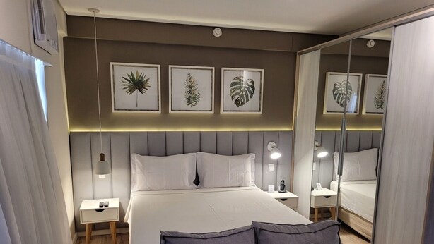A modern hotel room with a large bed, bedside tables, a sofa, and wall art. - Travel Inn Hotels Ibirapuera (São Paulo)