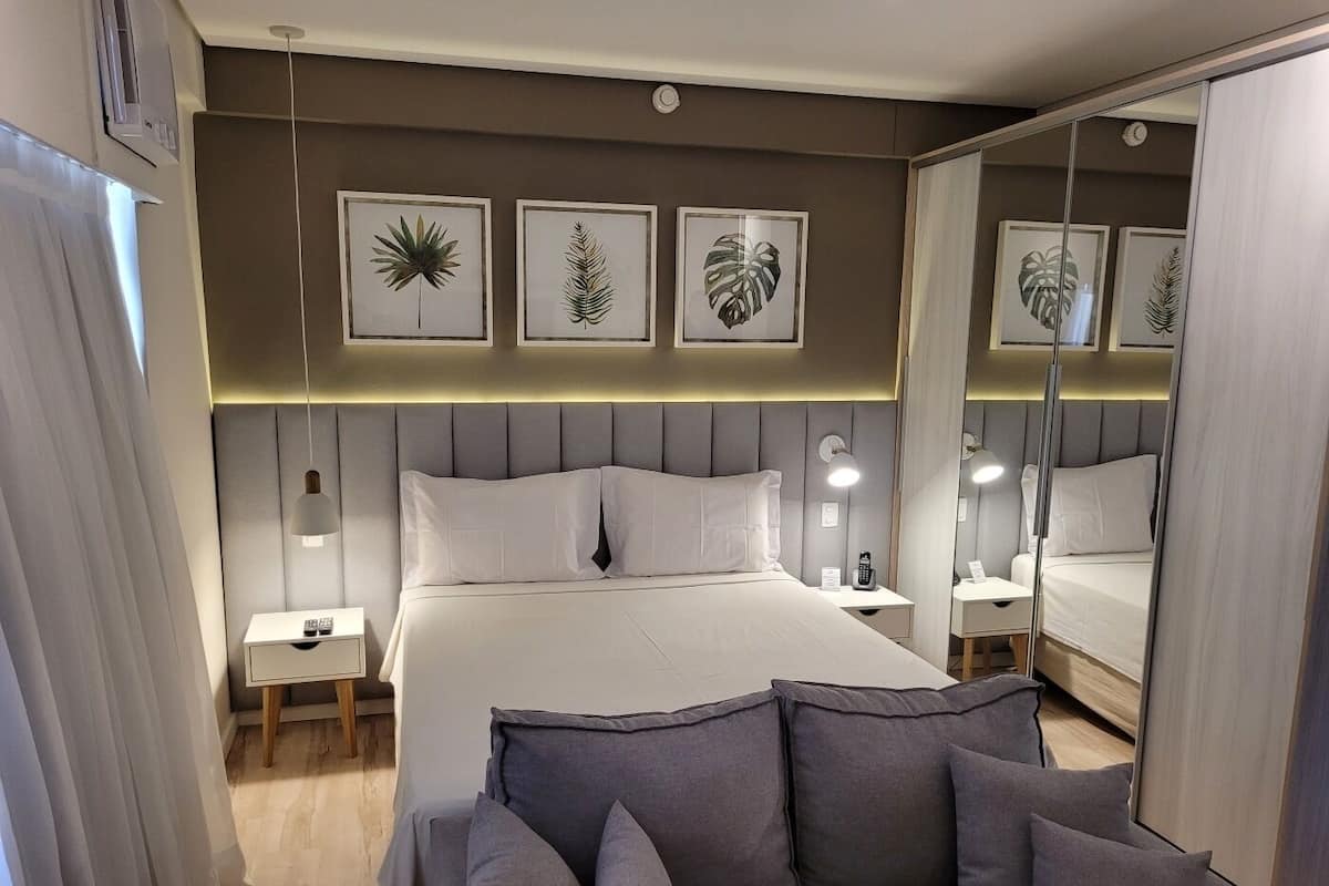 A modern hotel room with a large bed, bedside tables, a sofa, and wall art.