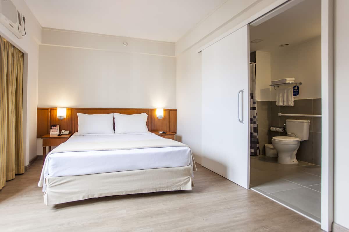 A hotel room with a large bed, bedside lamps, a nightstand, and a view into the bathroom.