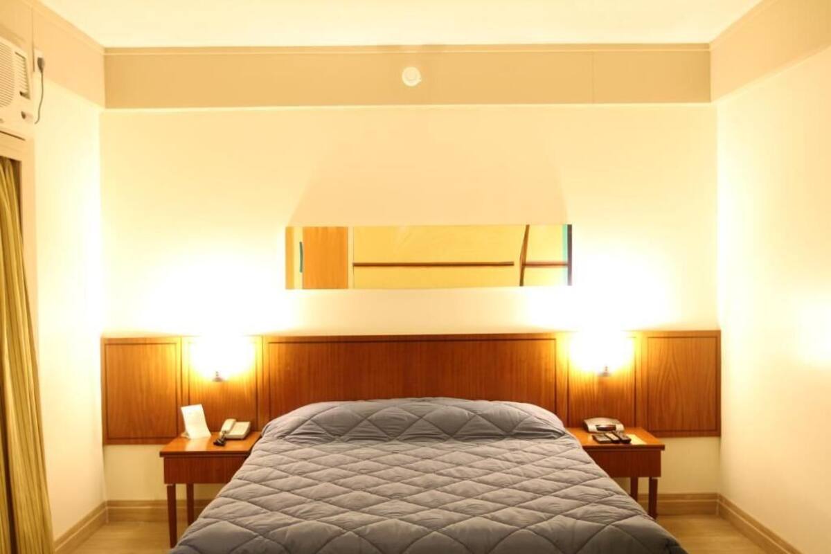 A hotel room with a large bed, two bedside tables with lamps, a mirror above the bed, and a ceiling light.