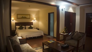 A hotel room with a large bed, two bedside tables, a nightstand, a sitting area with a coffee table, a sofa, and a small table with a vase of flowers. - GS Plaza Hotel (Accra)