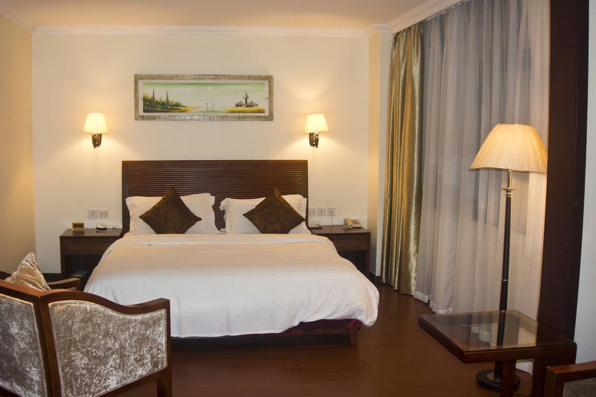 A hotel room with a large bed, two bedside tables, a chair, a lamp, and a painting on the wall.