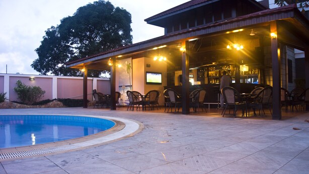 An outdoor pool area with a covered seating area, chairs, and a bar. - GS Plaza Hotel (Accra)