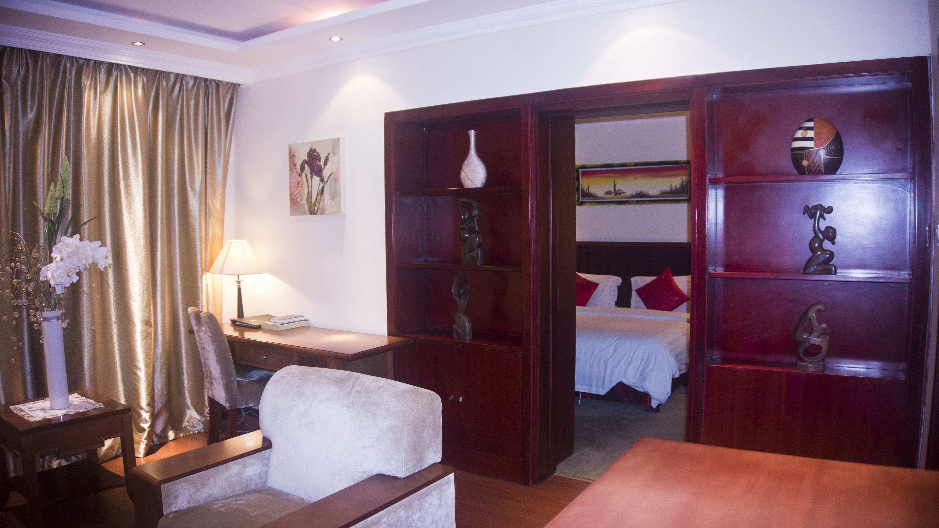 A hotel room with a bed, a desk, a chair, a bookshelf, and a decorative vase.
