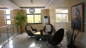 A modern lobby with a glass coffee table surrounded by unique chairs, large windows, and a potted plant. - GS Plaza Hotel (Accra)