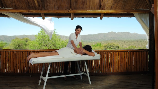 A person receiving a massage on a wooden deck with a view of mountains.