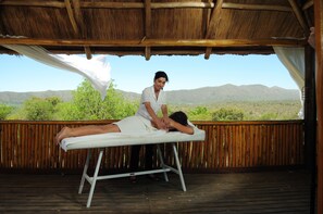 Une personne reçoit un massage sur une terrasse en bois, avec vue sur les montagnes.