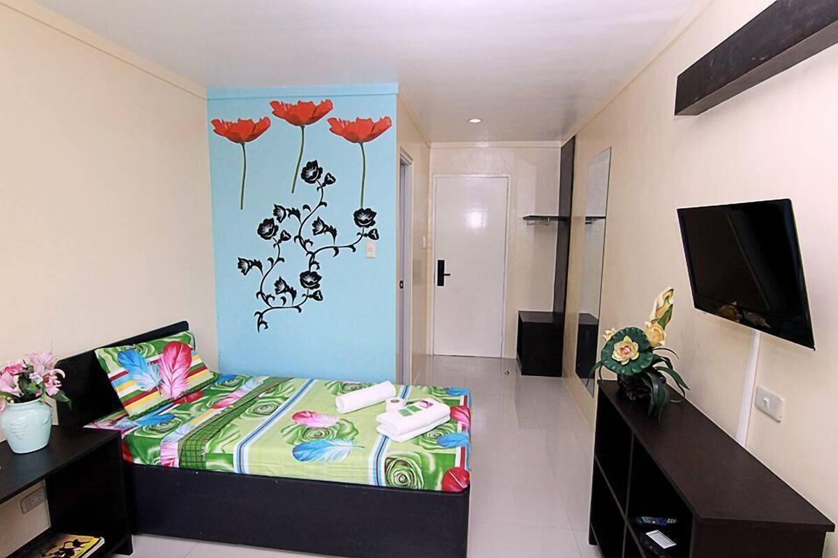 Habitación de hotel con cama, escritorio, televisión y un mural floral en la pared.