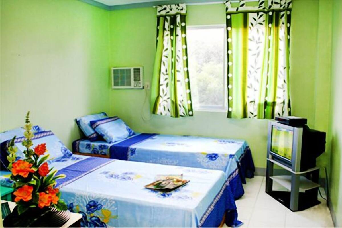 Habitación con dos camas, televisión y ventana con cortinas.
