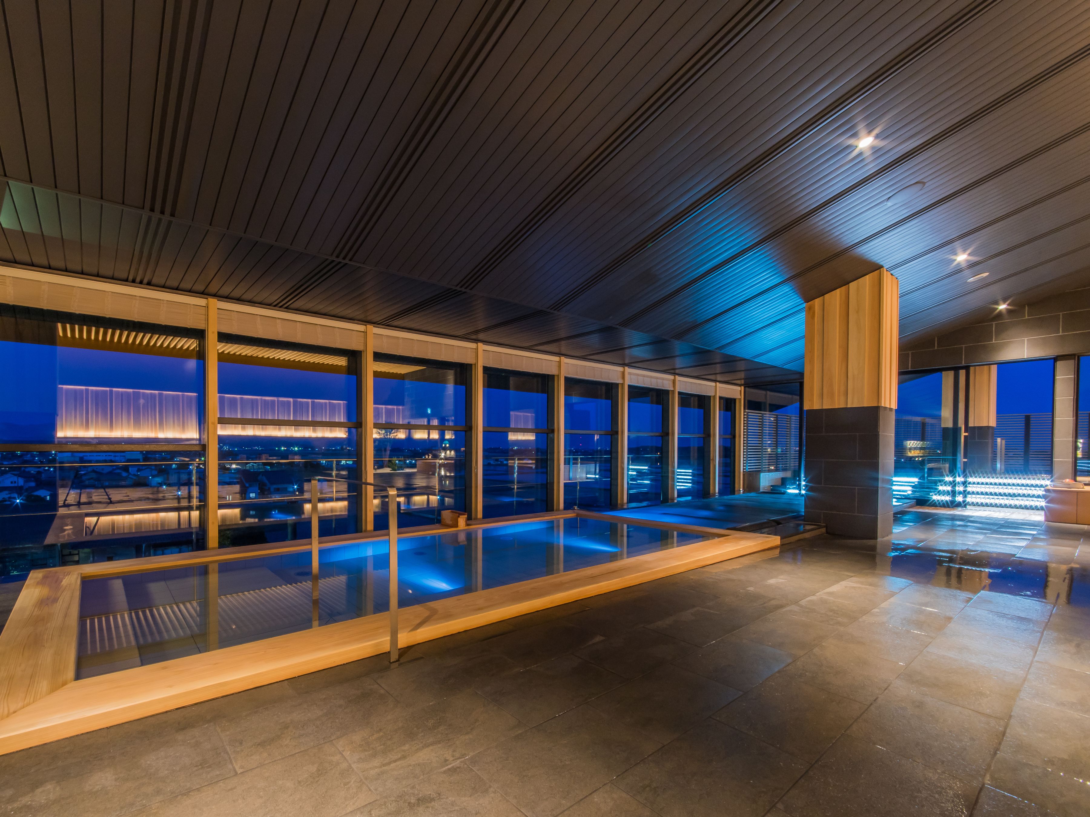 A modern indoor pool area with glass walls and a view of the cityscape at night.