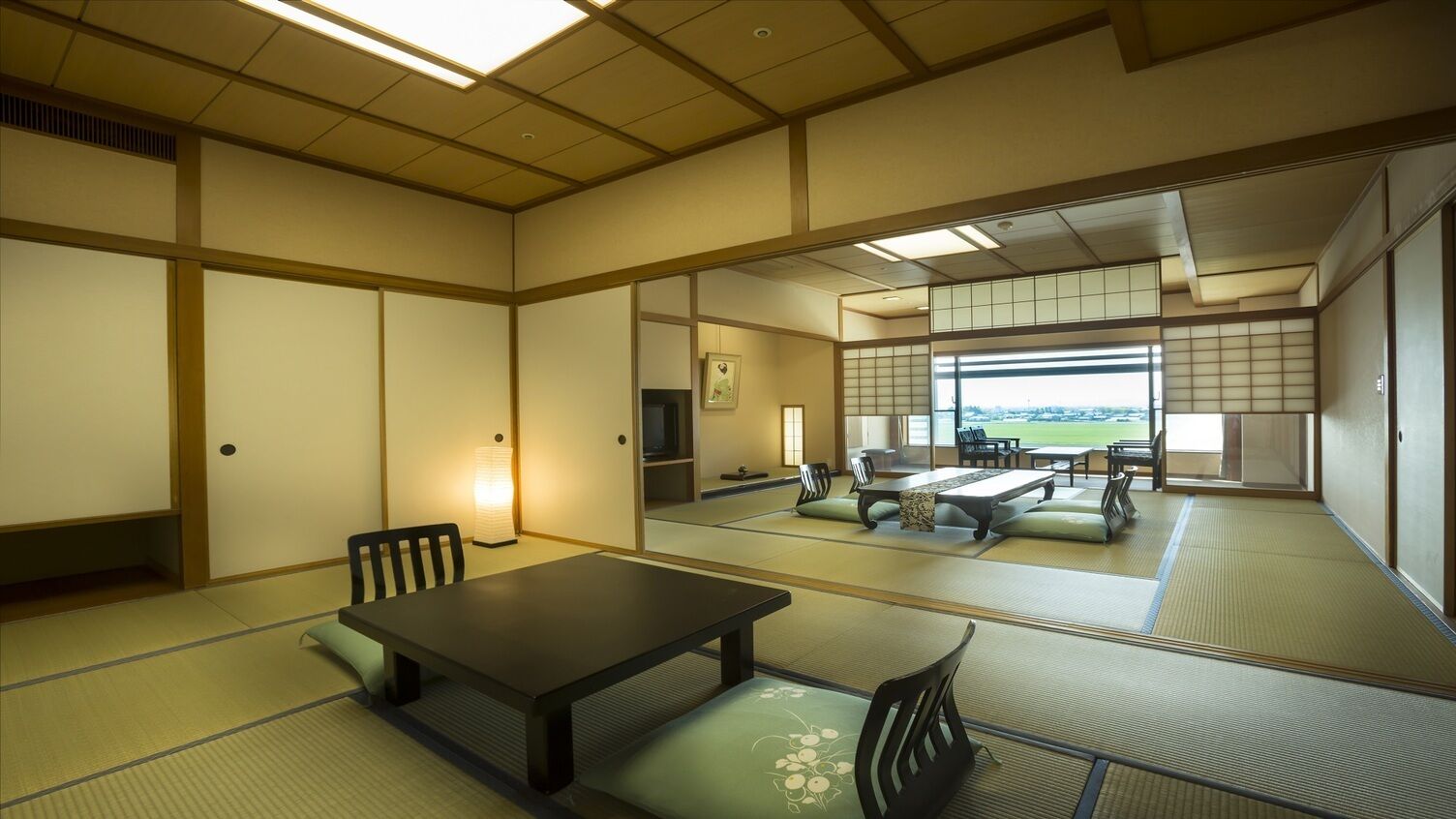 A tatami mat room with a low table and chairs, a sliding door, and a view of a green landscape.