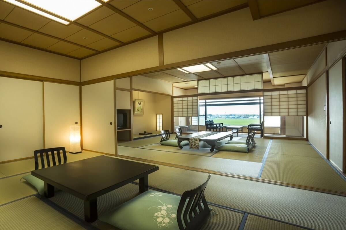 A tatami mat room with a low table and chairs, a sliding door, and a view of a green landscape.