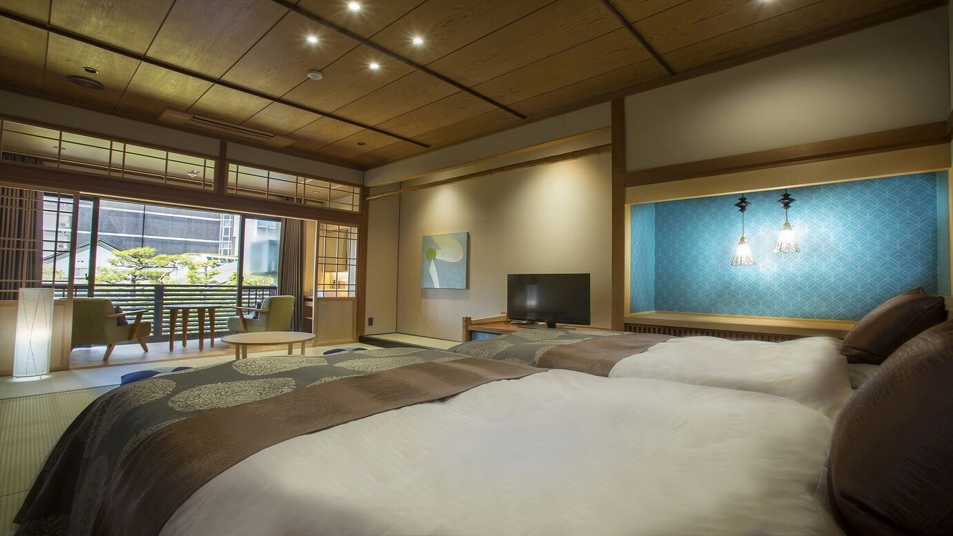 A hotel room with a large bed, a TV, a desk, and a view of a garden through the window.