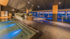 A modern indoor pool area with a bar and seating, large windows, and a high ceiling. - Grandia Housen (Awara)