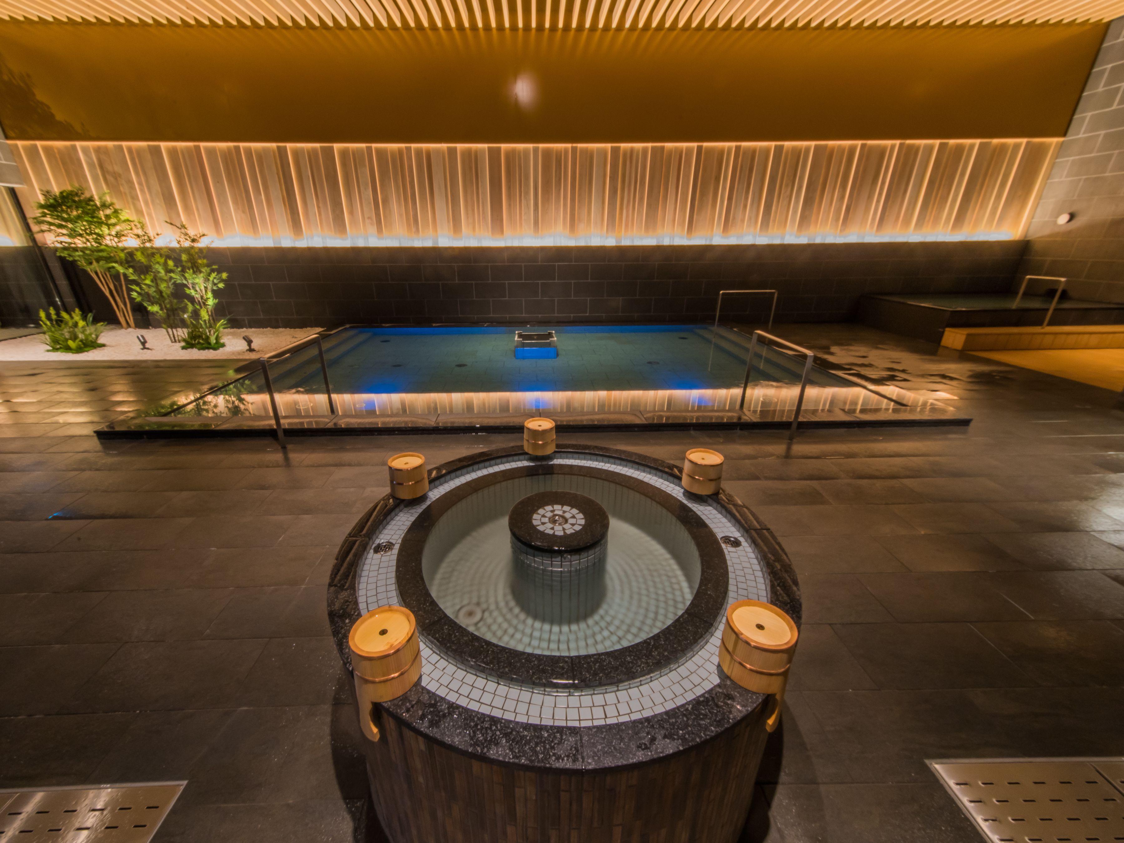 Un área de piscina interior moderna con un jacuzzi central, rodeado de suelo de baldosas y techo de madera.