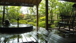 A wooden deck with a hot tub and a rocking chair, surrounded by lush greenery. - Grandia Housen (Awara)