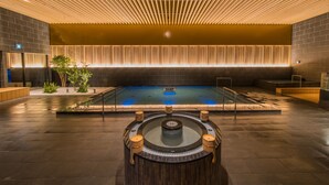 A modern indoor pool area with a central hot tub, surrounded by dark tiled flooring and wooden accents. - Grandia Housen (Awara)