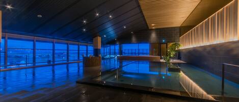 A modern indoor pool area with a glass barrier, large windows, and a wooden ceiling.